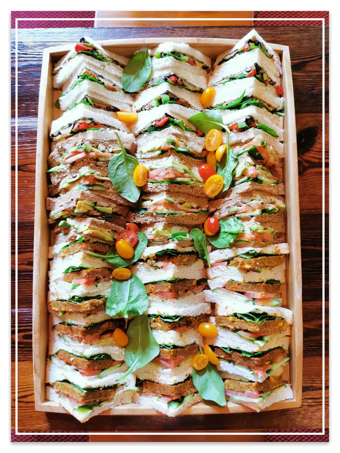 A wooden tray packed with triangle-cut sandwiches garnished with spinach and yellow tomatoes — Montgomery Street Cafe's sandwich platter.